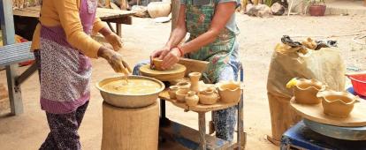 A Cambodian woman teaches a senior volunteer traditional Khmer pottery. An older volunteer participates in a pottery class as part of her Khmer cultural experience in Cambodia.